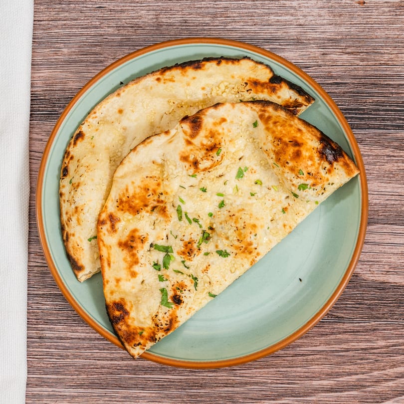 Two pieces of golden-brown Indian naan bread, garnished with herbs, on a light blue plate.