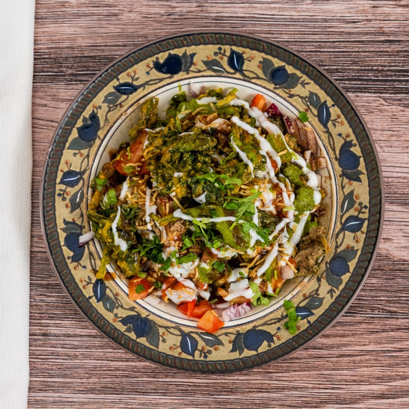 Overhead view of Indian chaat with green chutney, yogurt, and fresh cilantro on a decorative plate.