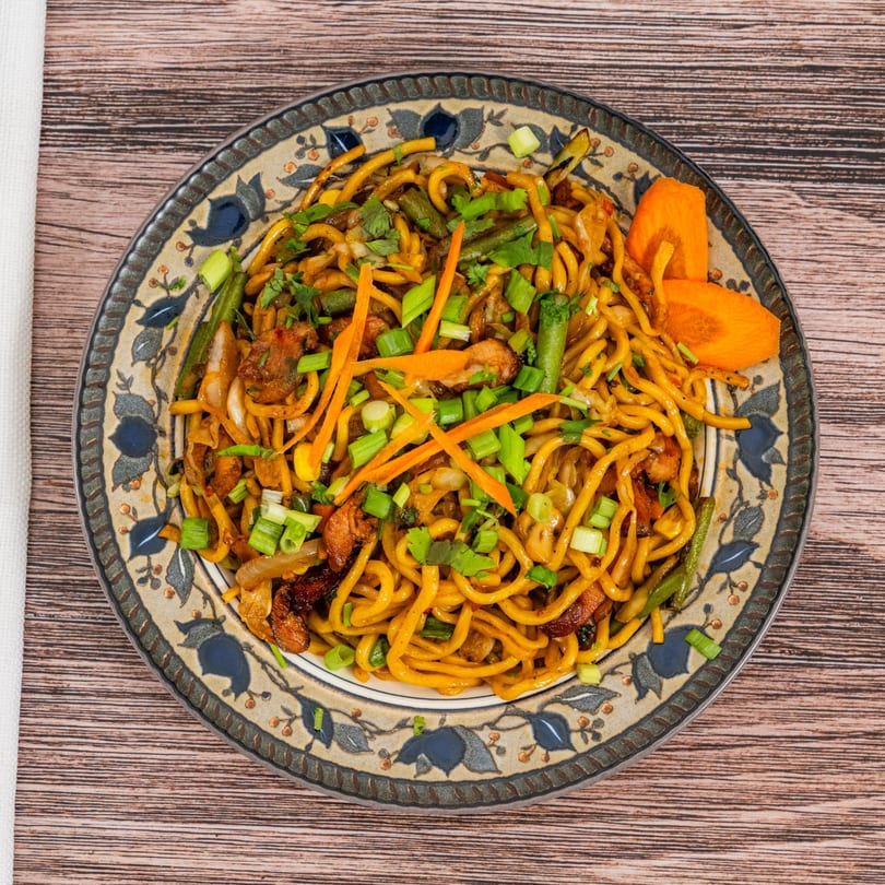 Moh Moh Licious's Indian noodles with vegetables, chicken, and fresh herbs on a decorative plate.